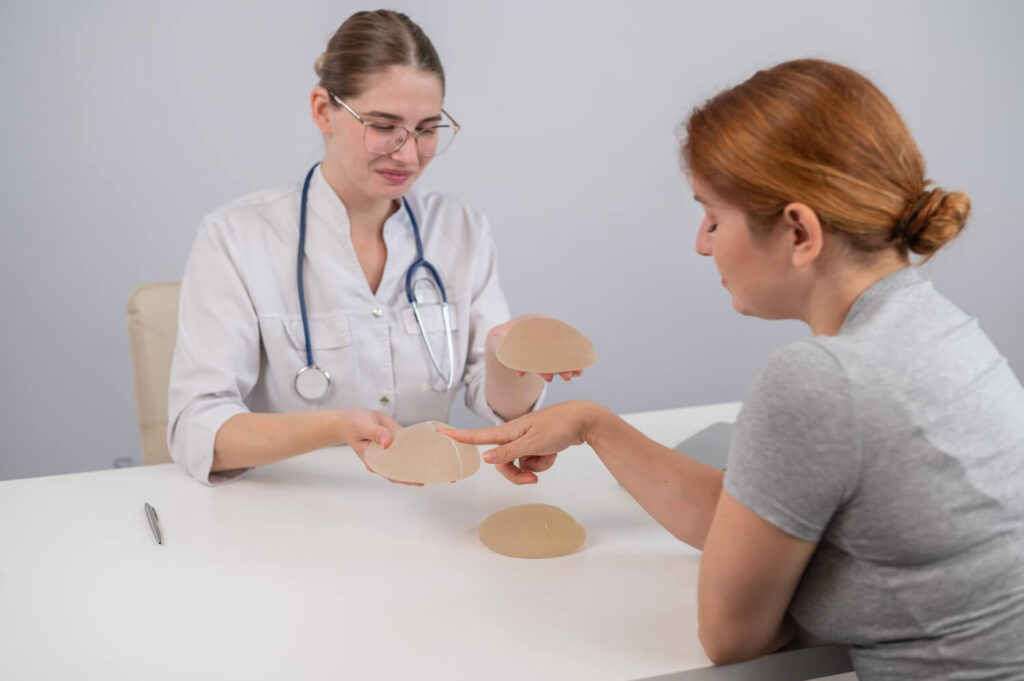 Médica e paciente feminina à mesa do consultório analisando tipos de prótese mamária